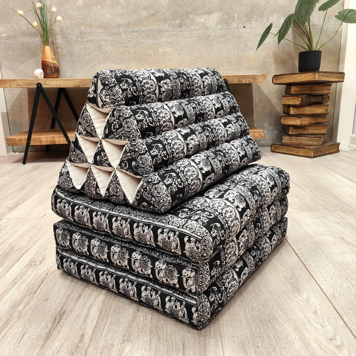 Stack of black and white patterned cushions on a wooden floor with a neutral wall background.